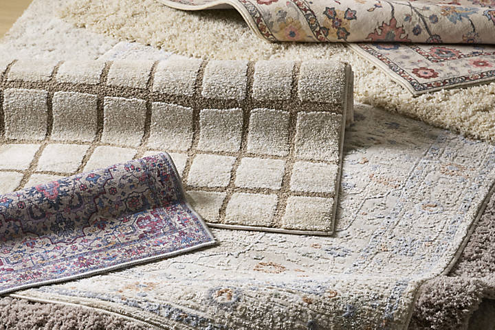Add a layer of comfort and style to your home with our new range of rugs. A close up image of our collection of new rugs with various patterns: checkered, floral, and geometric designs in neutral and pastel colors, suggesting a cozy ambiance.